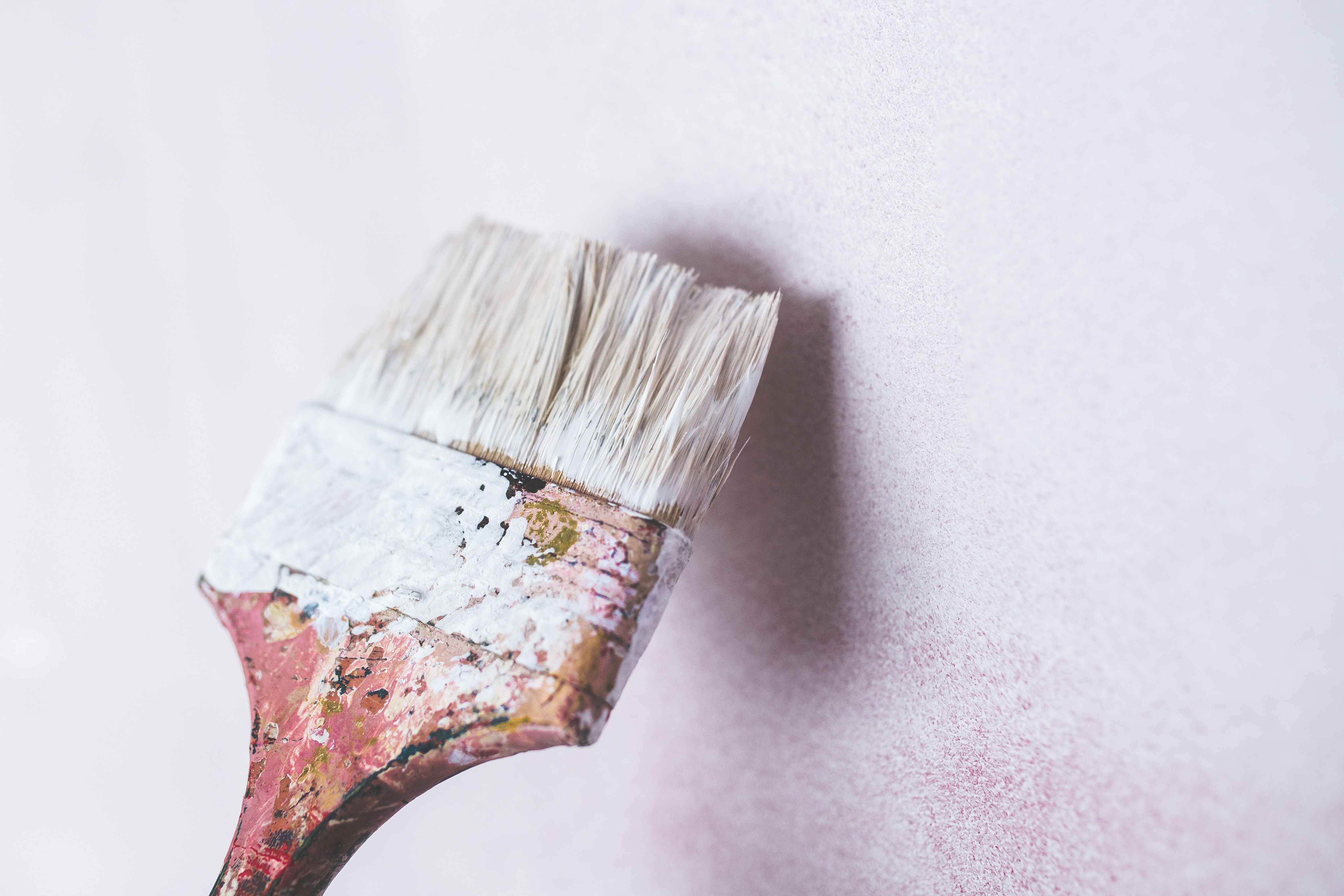 Close-up of a paintbrush with white paint against a soft pink wall, symbolizing painting and decorating tasks.