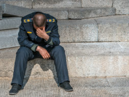 Sad policeman is sitting on the floor with his had down, he lost his job, he is alone.
