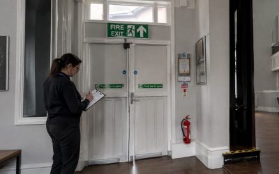 a staff member checking a clipboard near a clearly marked fire exit sign.